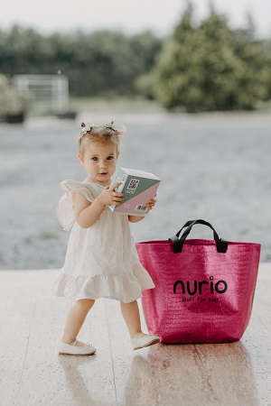fetita care tine in mana o cutie a unui joc si are in preajma ei o plasa roz cu inscriptia Nurio