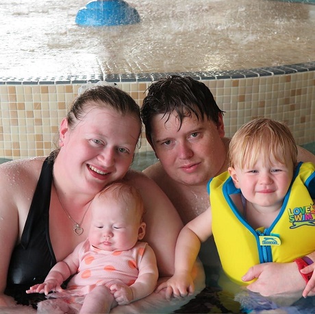 parinti fericiti alaturi de copiii lor la o piscina