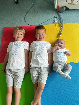 doi baietei si un bebelus stand toti trei intinsi pe un covoras format din patrate colorate