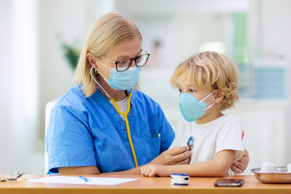 doctorita care poarta masca de protectie si consulta un copil ce poarta si el masca de protectie
