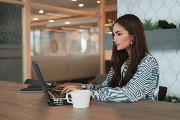 femeie tanara care sta la birou si lucreaza folosind un laptop