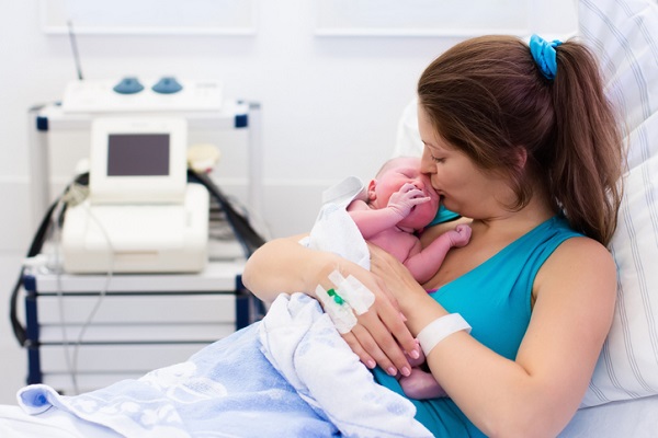 mama care sta in pat, la spital, si isi saruta bebelusul nou-nascut