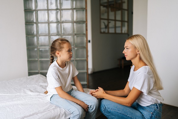 fetita trista care sta pe pat si mama care incearca să discute cu ea