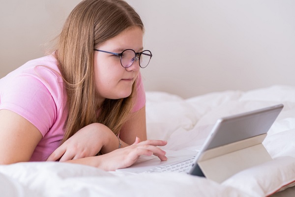 adolescenta in tricou roz care sta in pat si se uita pe o tableta