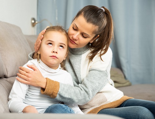 mama care sta pe canapea langa fetita ei si incearca sa o consoleze dupa un moment tensionat