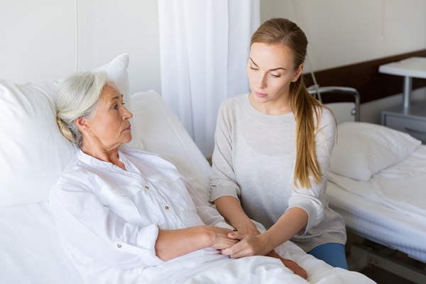 femeie tanara care îi este alaturi mamei sale aflate pe patul de spital