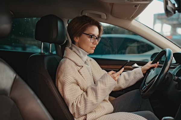 femeie cu ochelari si haina groasa eleganta, stand in masina si uitandu-se pe telefon