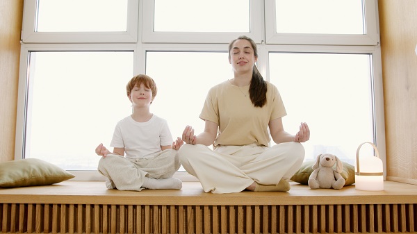 mama si baietelul ei care fac yoga acasa, langa fereastra