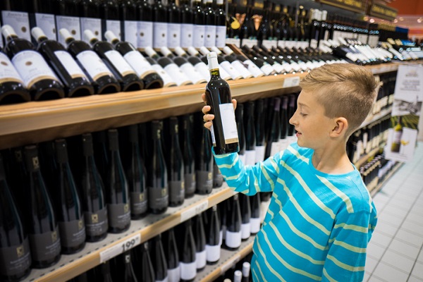 adolescent aflat la un stand de vinuri, tinand in mana o sticla de vin