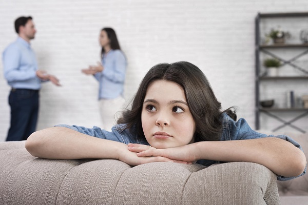 adolescenta stand trista pe canapea in timp ce parintii ei se cearta