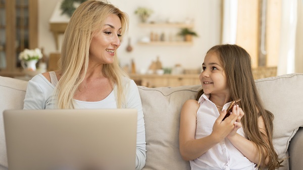 mama care are laptopul in fata si discuta cu fetita ei, zambitoare, care tine in mana un telefon