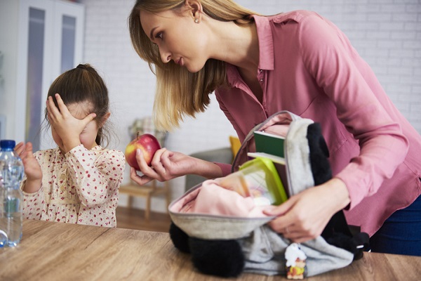 fetita care isi acopera fata cu mainile cand mama ei vrea sa-i puna un mar pentru gustarea la scoala