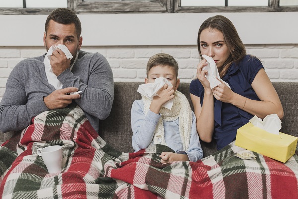parinti si baietelul lor stand in pat si suflandu-si nasul din cauza unei infectii respiratorii