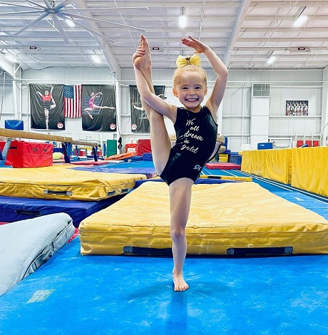 fetita blonda vesela, care se antreneaza intr-o sala de gimnastica