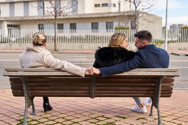 triunghi amoros, doua femei si un barbat care stau pe o banca