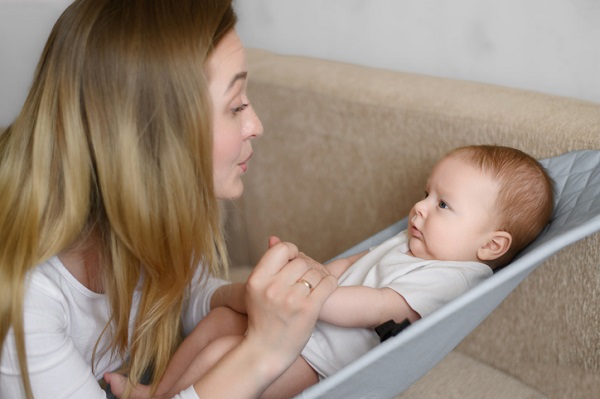 mama care isi tine bebelusul de manuta si se uita la el in timp ce îi vorbeste