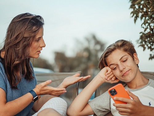 mama care incearca sa discute cu fiul ei adolescent in timp ce acesta o ignora stand pe telefon