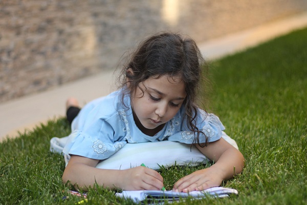 fetita care sta intinsa pe iarba si noteaza ceva intr-un jurnal