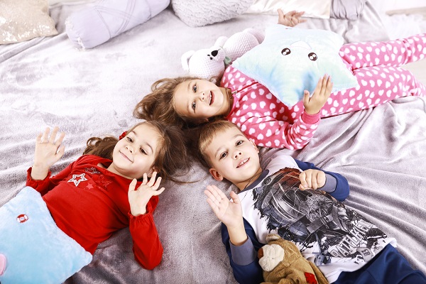 trei copii in pijamale stand intinsi pe pat