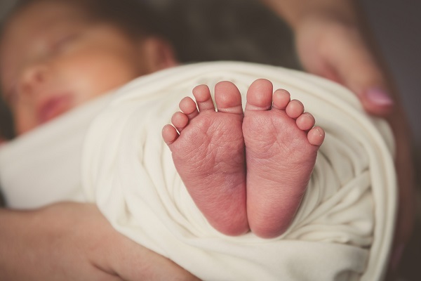 femeie alaturi de un bebelus invelit intr-o paturica alba, cu piciorusele goale