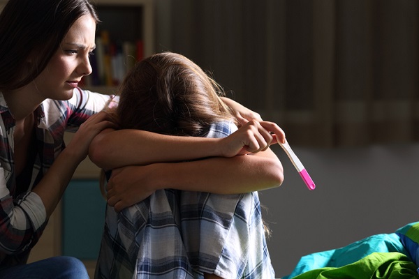 tanara care consoleaza o adolescenta care plange si tine in mana un test de sarcina