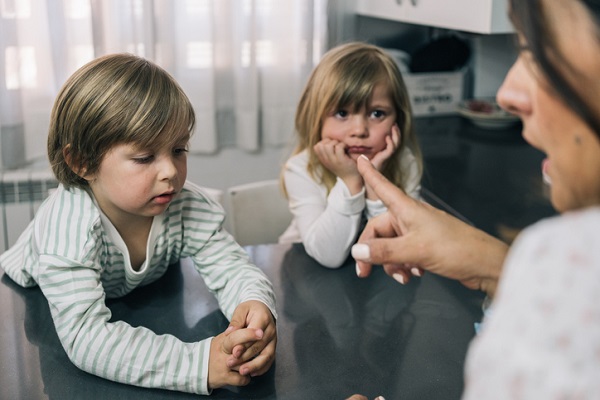 mama care incearca sa isi disciplineze copiii ce stau sprijiniti de o masa