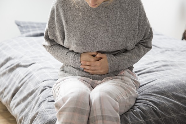 femeie care sta pe marginea patului suferind din pricina disconfortului abdominal