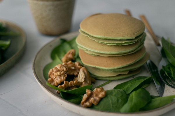 clatite pancakes cu spanac pe o farfurie pe care se afla miez de nuca si frunze proaspete de spanac