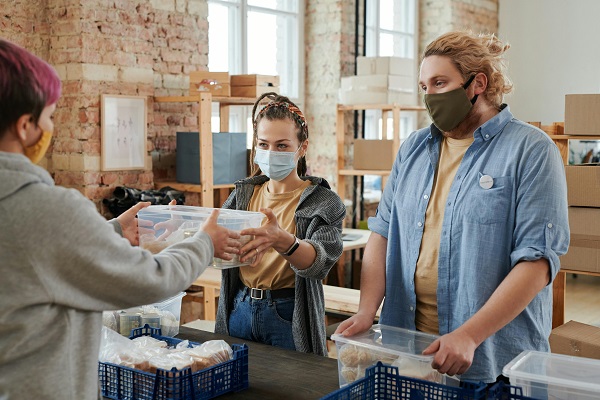 tineri cu masti de protectie ce fac voluntariat la un centru de donatii de alimente