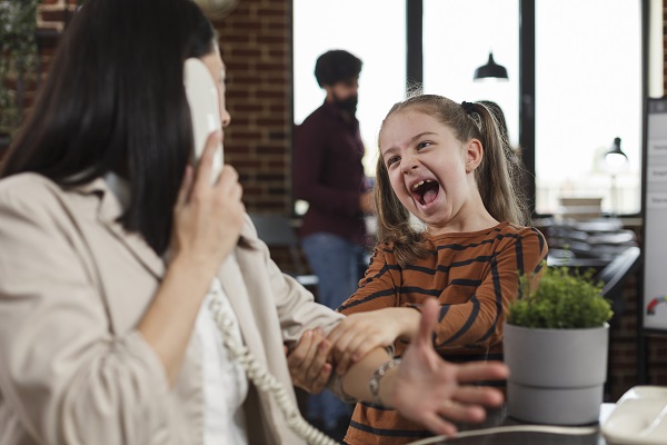 fetita care isi deranjeaza mama ocupata la birou, care vorbeste la telefon