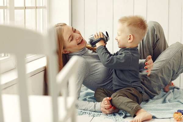 mama care sta intinsa pe jos in timp ce se joaca cu baietelul ei