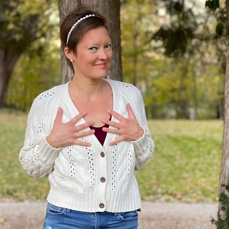 femeie tunsa scurt, cu pulover si blugi, ducandu-si mainile pe piept