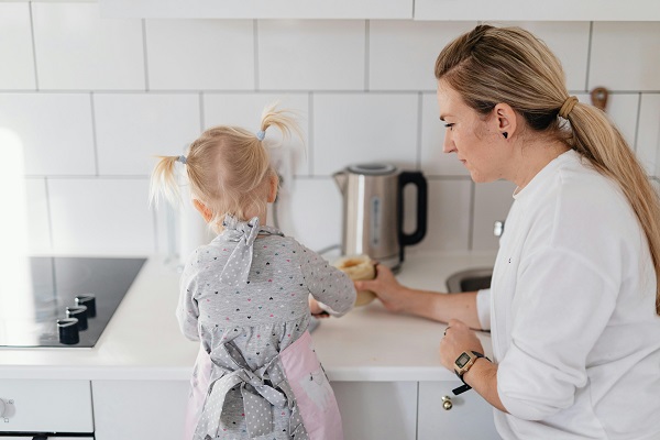 mama care sta langa fetita ei in bucatarie in timp ce aceasta incearca sa-si prepare ceva de mancare