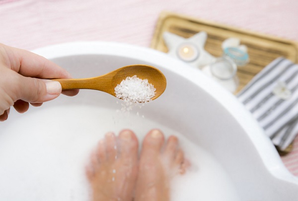 femeie care se pregateste sa toarne sare dintr-o lingurita pentru o baie la picioare