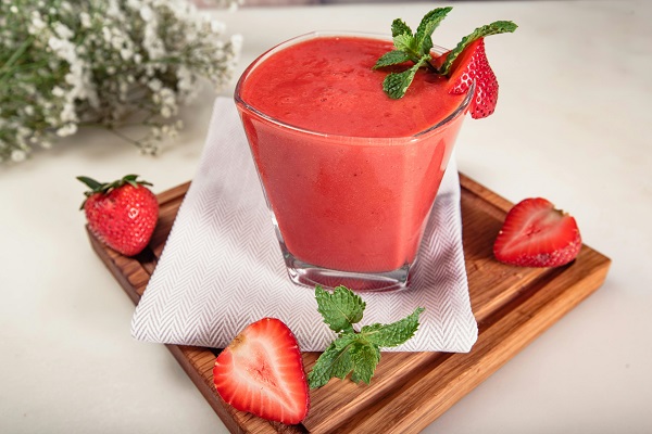 pahar cu smoothie de capsuni, decorat cu o capsuna proaspata si cu o frunza de menta