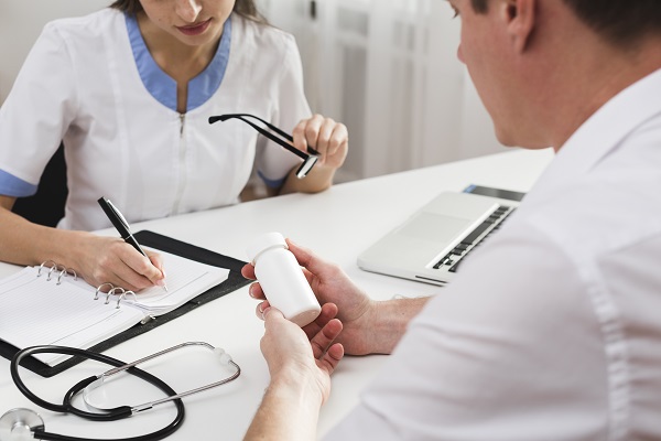 barbat care tine in mana un flacon de medicamente in timp ce se afla in cabinetul medical