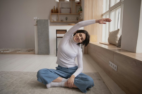 femeie tanara, zambitoare, incercand sa faca un exercitiu yoga intr-o camera a casei 