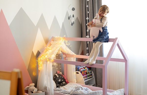 fetita care se joaca in camera ei, cocotata pe cadrul patutului in forma de casuta