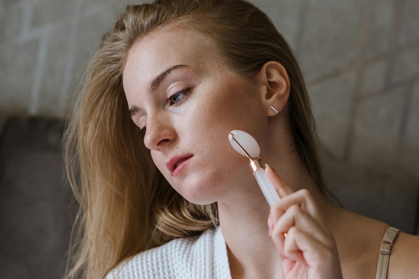 femeie tanara care isi maseaza fața cu ajutorul unei role pentru masajul facial