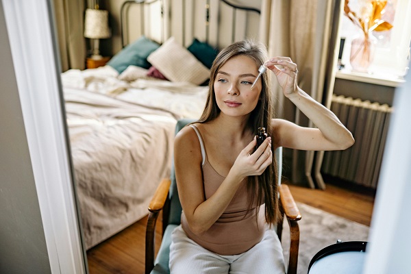 femeie tânără care stă în fața oglinzii și se pregătește să utilizeze un ser facial
