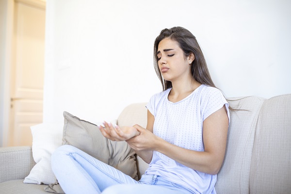 femeie tânără care stă pe canapea și suferă de dureri la nivelul încheieturii