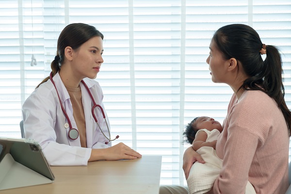 doctorita stând de vorba la consultatie cu o mama care isi tine bebelusul in brate