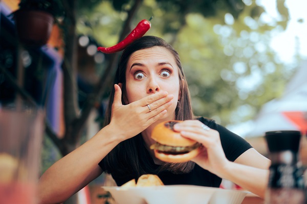 femeie tânără care a pus mâna la gură după ce a mușcat dintr-un burger picant