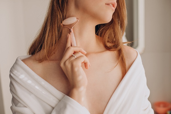 femeie care isi face masaj cu o rola de masaj facial de cuarț roz