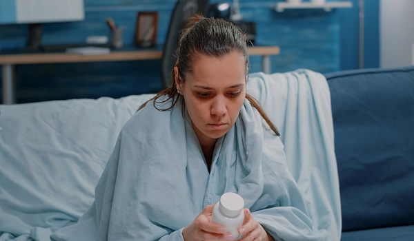 femeie bolnavă care stă pe pat și se uită la un flacon cu medicamente