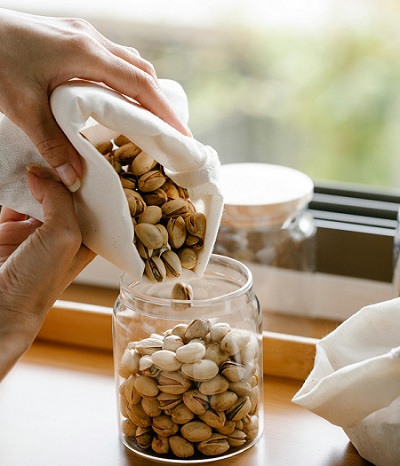 femeie care tine in mana o punga alba in care se afla fistic pe care il toarna intr-un borcan de sticla