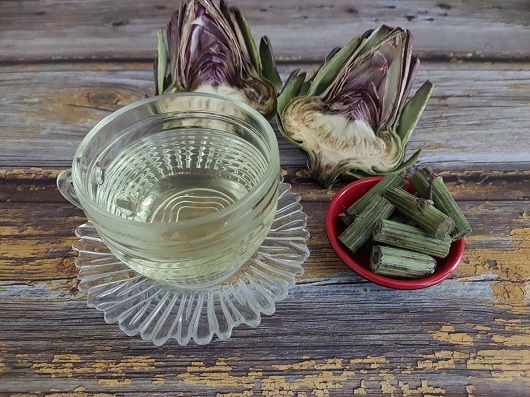 cana de sticla cu ceai de anghinare, pusa pe o farfurie tot de sticla, langa cana aflandu-se o anghinare proaspata taiata pe jumatate si un castronel rosu pe care se afla bucati de tulpina de anghinare