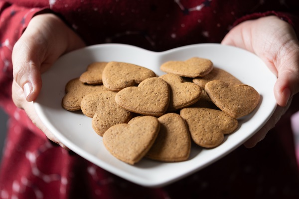 maini de femeie care tin un castron alb, in forma de inima, in care se afla turta dulce in forma de inimioare