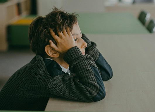 baietel deprimat, imbracat in pulover maro cu negru, tinandu-si capul in maini in timp ce isi sprijina coatele de o masa intr-un spatiu interior