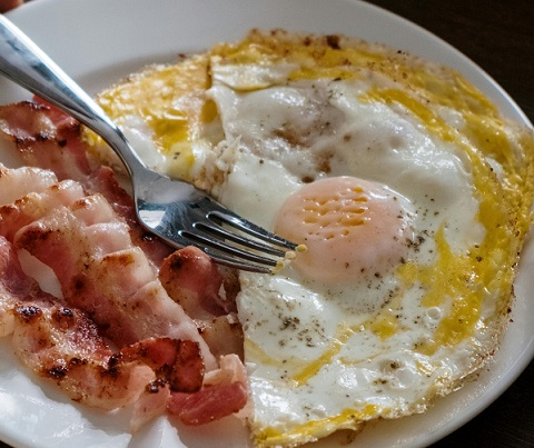 oua si felii de sunca rumenita puse pe o farfurie alba, cu furculita